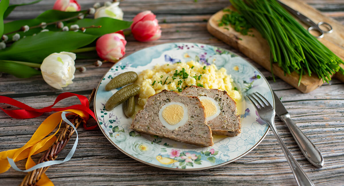 Sekaná s vajíčkem nakrájená na dva plátky na talíři s bramborovou kaší